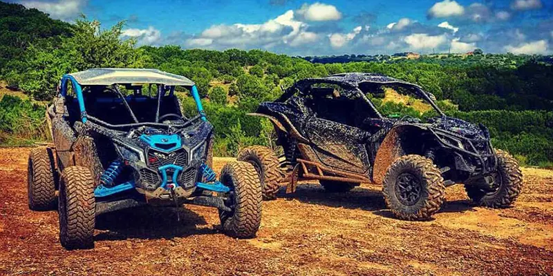 A side-by-side parked on a trail overlooking a vast Texas Hill Country valley at sunset.
